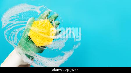 Banner der Bereinigung. Eine Hand in Gummihandschuhen wischt das Glas mit einem Schaumschwamm ab. Blauer Hintergrund mit Kopierbereich. Das Konzept der professionellen Reinigung s Stockfoto