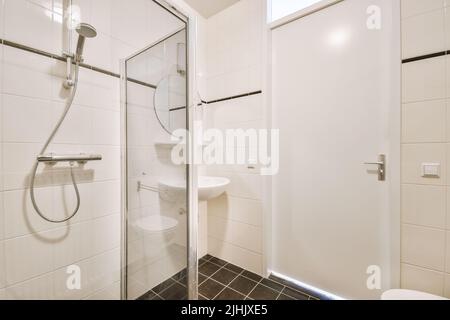 Badewanne mit Glasdusche in der Ecke neben Waschbecken und Toilette im kleinen hellen Badezimmer mit weißen Kachelwänden Stockfoto