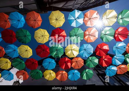 19. Juli 2022, Hessen, Büdingen: In der Altstadt scheint die Sonne zwischen dutzenden bunten Schirmen, die sich dort zwischen den Häusern zu einer Installation ausgestreckt haben. An einigen Stellen werden die Temperaturen voraussichtlich auf 40 Grad steigen. Foto: Boris Roessler/dpa Stockfoto