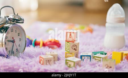 Seine Babyzeit. Stillleben von einer Uhr, Spielzeug und einer Babyflasche auf einer flauschigen Matte. Stockfoto