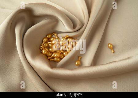 Goldene Kapseln des Gesichts-Serums oder ätherisches Öl für die Gesichtsmassage liegen auf einem beigen Stoff Stockfoto