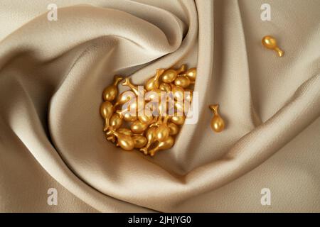 Goldene Kapseln des Gesichts-Serums oder ätherisches Öl für die Gesichtsmassage liegen auf einem beigen Stoff Stockfoto