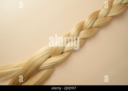 Das lange blonde Haar der Frau in Form der auf beigem Hintergrund liegenden Tress Stockfoto