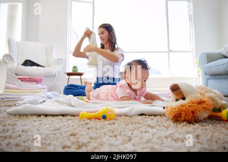 Whos mein Lieblingsmädchen. Eine Mutter faltet Kleidung, während ihr Baby in der Lounge spielt. Stockfoto