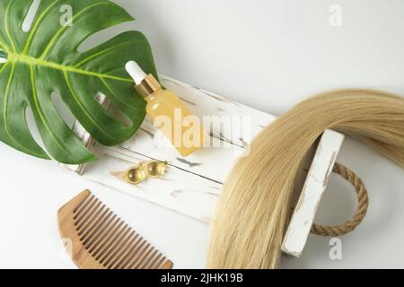 Ein natürliches ätherisches Öl oder Serum für die Haarpflege in goldenen Kapseln, die auf einem weißen Tisch liegen. Haarpflege und Glättung Konzept Stockfoto
