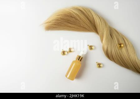 Ein natürliches ätherisches Öl oder Serum für die Haarpflege in goldenen Kapseln, die auf einem weißen Tisch liegen. Haarpflege und Glättung Konzept Stockfoto
