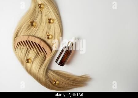 Ein natürliches ätherisches Öl oder Serum für die Haarpflege in goldenen Kapseln, die auf einem Strang blondes Haar liegen. Haarpflege und Glättung Konzept Stockfoto