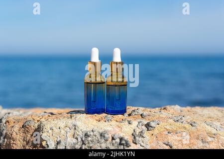 Natürliche ätherische Öle oder Serum in Tropfflaschen, die auf den Steinen am Meer stehen Stockfoto