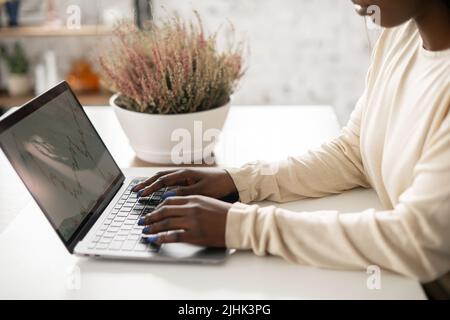 Beschnittene Ansicht der weiblichen Hände, die auf dem Laptop tippen. Afrikanische Frau mit Laptop mit Grafiken auf dem Bildschirm Stockfoto