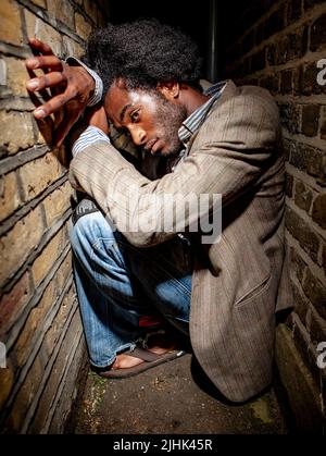 Urbane Angst. Ängstliche Körpersprache eines verletzlichen Charakters, der in einer dunklen und engen Gasse gefangen ist. Aus einer Bildserie mit dem gleichen Modell. Stockfoto