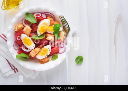 Toskanischer Panzanella-Salat. Frischer Tomaten-Salat mit Basilikumblättern, Eiern, Olivenöl und Zwiebeln in einer weißen Schüssel auf hellem Hintergrund. Vegetarische Panzanella sa Stockfoto