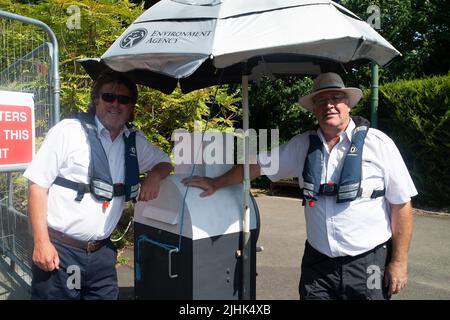 Bray, Großbritannien. 19.. Juli 2022. Die Schleusenwärter von Bray Lock bekommen etwas Schatten unter einem Regenschirm. Schwanenboot auf der Themse bei Bray Lock. Swan Upping ist die traditionelle britische jährliche Zählung der Schwäne und Cygnets an der Themse durch die Royal Swan Uppers und Swan Uppers der Lackhersteller der Winzer und Dyers. Quelle: Maureen McLean/Alamy Live News Stockfoto