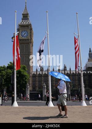 Ein Mann nutzt einen Regenschirm, um sich vor der Sonne zu schützen, während er an den Houses of Parliament, Westminster, vorbeigeht. Die Temperaturen haben in Großbritannien zum ersten Mal 40C erreicht, wobei 40,2C vorläufig in London Heathrow aufgezeichnet wurden, teilte das Met Office mit. Bilddatum: Dienstag, 19. Juli 2022. Stockfoto