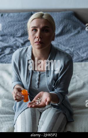 Verärgert blonde Frau mit Wechseljahren hält Flasche und Pillen in den Händen Stockfoto