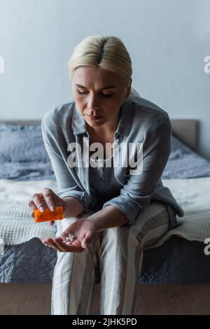 Verärgert blonde Frau mit Wechseljahren hält Flasche und Gießen Pillen in der Hand Stockfoto