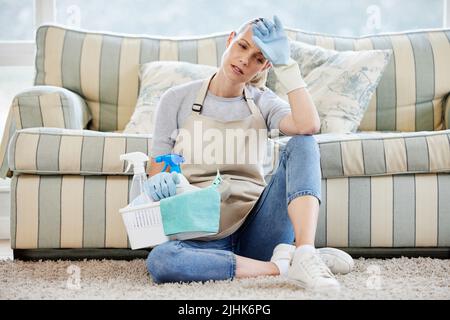 Hausarbeit... die nie endende Aufgabe. Eine junge Frau, die erschöpft aussieht, während sie zu Hause Hausarbeiten macht. Stockfoto