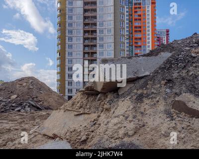 Eine Baustelle mit Sandhaufen, riesigen Betonblöcken und Bauabfällen im Vordergrund und neuen Hochhäusern im Hintergrund in Kiew. Stockfoto