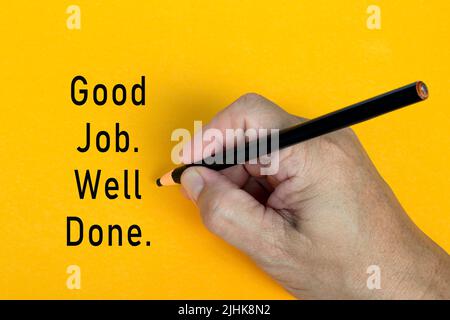 Männliche Hand schreibt in schwarzem Bleistift das Wort GUTE ARBEIT GUT GEMACHT auf einem gelben Hintergrund. Ermutigende Worte und Geschäftskonzept. Stockfoto