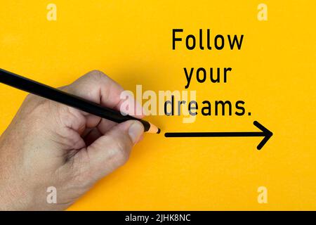 Männliche Hand schreibt in schwarzem Bleistift das Wort FOLLOW YOUR DREAMS auf einem gelben Hintergrund. Ermutigende Worte und Geschäftskonzept. Stockfoto