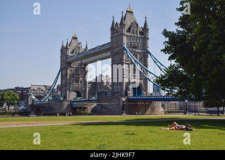 London, England, Großbritannien. 19.. Juli 2022. Neben der Tower Bridge liegt ein einbunter Sonnenanbeter, während das Vereinigte Königreich mit über 40 Grad Celsius die höchsten Temperaturen aller Zeiten verzeichnet. Das Met Office hat seine erste rote Warnung vor extremer Hitze in Großbritannien veröffentlicht. (Bild: © Vuk Valcic/ZUMA Press Wire) Stockfoto