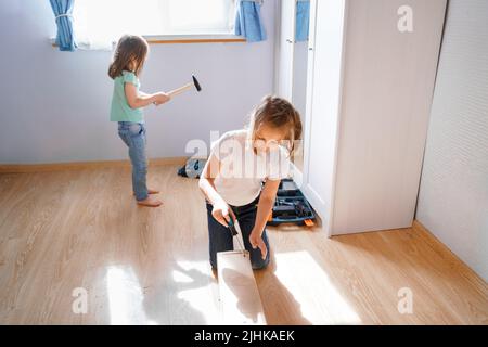 Papa, kleine Mädchen Töchter, die nach den Anweisungen im Kinderzimmer ein hölzernes Babybett zusammenstellen. Vater helfen, Kindermöbel montieren. Selbstbedienung Stockfoto