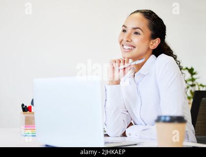 Ich kann es kaum erwarten, erfolgreich zu sein. Eine attraktive junge Geschäftsfrau, die allein im Büro sitzt und besinnlich aussieht, während sie ihren Laptop benutzt. Stockfoto