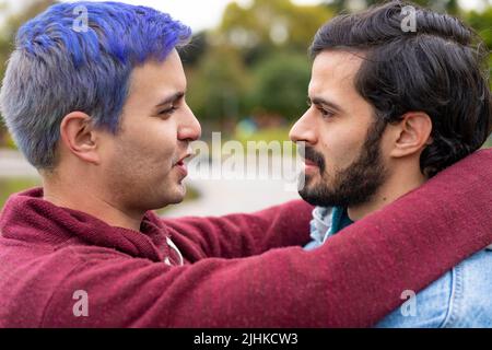 Lateinisches schwules Paar umarmt sich in einem Park und schaut sich an, wie es sich küssen wird Stockfoto