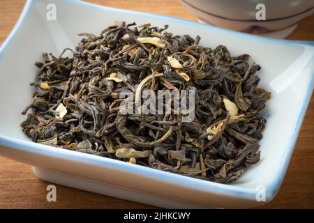 Getrocknete chinesische Jasminteeblätter aus der Nähe in einer Schüssel auf einem hölzernen Hintergrund Stockfoto