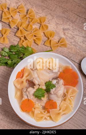 Makkaroni-Suppe mit Hühnerschenkeln in klarer Brühe mit Karotten.auf rustikalem, altem Holzhintergrund. Stockfoto