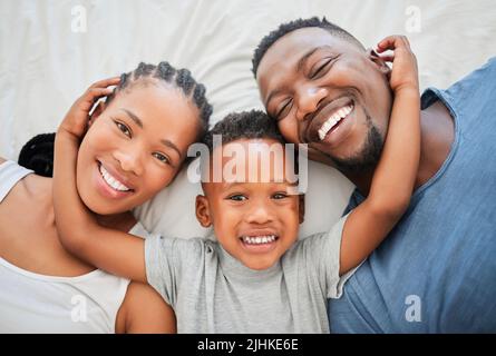 Aufwachen zu einem hellen und schönen Tag. Aufnahme einer glücklichen Familie, die sich zu Hause auf einem Bett entspannt. Stockfoto