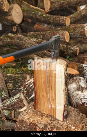 Eine spezielle Axt zum Spalten von Holz wird in den Baumstamm geklebt. Die Axt teilt das Log für die Trocknung und die anschließende Vorbereitung für den Heizschrott im Winter. Stockfoto