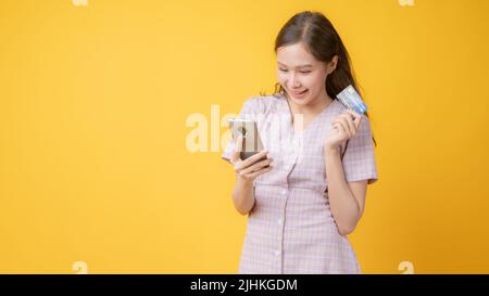 Junge asiatische Frau in rosa Kleid hält Telefon auf gelbem Hintergrund Stockfoto