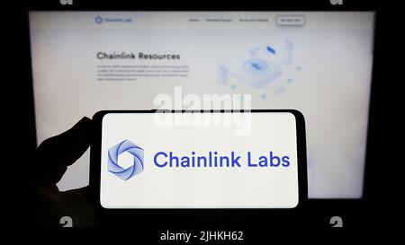 Person, die das Smartphone mit dem Logo des US-Blockchain-Unternehmens Chainlink Labs auf dem Bildschirm vor der Website hält. Konzentrieren Sie sich auf die Telefonanzeige. Stockfoto