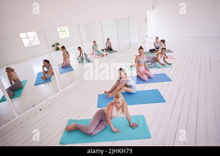 Gruppe von Frauen, die sich im Yoga-Kurs ausruhen. Junge Frauen, die eine Pause vom Pilates-Kurs machen. Flexible Frauen, die sich während des Yoga-Kurses entspannen. Frauen sitzen auf dem Stockfoto