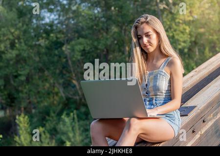 Konzentrierte junge Frau, die online als Grafikdesignerin auf ihrem Laptop arbeitet, umgeben von Natur und Kopierraum Stockfoto