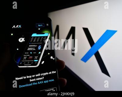 Person, die Mobiltelefon mit der Webseite des Kryptowährungsunternehmens AAX Limited auf dem Bildschirm vor dem Logo hält. Konzentrieren Sie sich auf die Mitte des Telefondisplays. Stockfoto