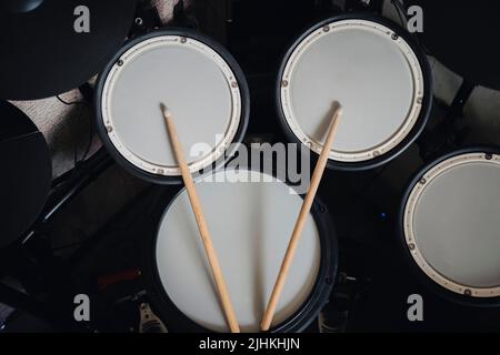 Drum-Ansicht eines elektronischen Drumkits mit Becken und Trommeln und einem Paar hölzernen Drumsticks, auf schwarzem Hintergrund. Konzept des Schlagzeuginstruments. Stockfoto