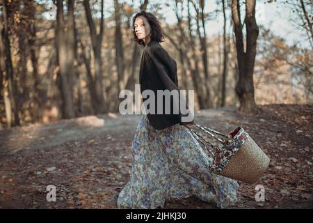 Porträt einer jungen Frau mit Vintage-Kleidung und einem Blumenkorb, die im Herbstpark spazieren geht Stockfoto