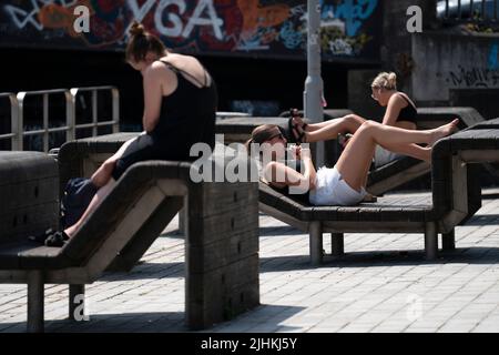 Manchester, Großbritannien. 19.. Juli 2022. Menschen sonnen sich im Zentrum von Manchester, Großbritannien, 19. Juli 2022. Ein Großteil des Vereinigten Königreichs (UK) war am Montag von sengenden Wetterverhältnissen ergriffen, ohne sich vor Mitte dieser Woche von der schwungenden Wärmeprognose zu erwärmen. Die Behörden haben vor Reiseunterbrechungen gewarnt und vorgeschlagen, in den kommenden Tagen von zu Hause aus zu arbeiten. Quelle: Jon Super/Xinhua/Alamy Live News Stockfoto