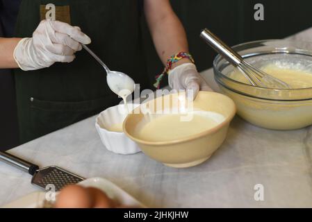 Hände in Gummihandschuhen, die Eigelb in einer Schüssel rühren Stockfoto