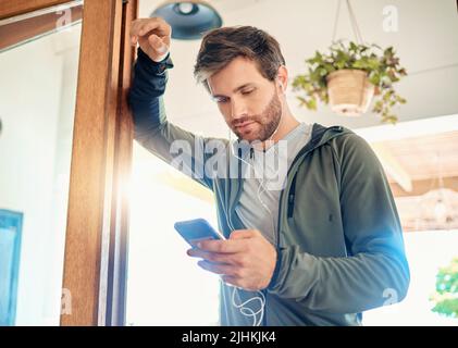 Ein junger Kaukasier hörte Musik mit Kopfhörern von einem Handy, während er eine Pause von der Übung zu Hause nahm. Guy SMS und Verwendung Stockfoto