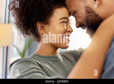 Glückliches gemischtes Rennpaar umarmt sich beim Entspannen zu Hause. Unbeschwerte hispanische Ehemann und Ehefrau lächeln, während sie einander liebevoll und in die Augen starren Stockfoto