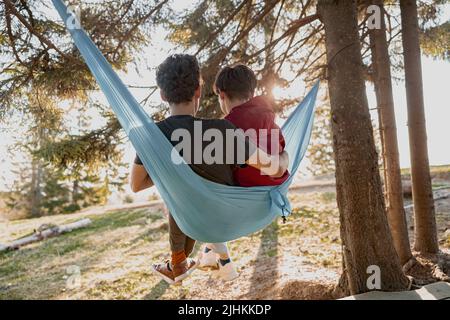 Hinten auf Paar sitzen und umarmen in der Hängematte im Wald. Mann und Frau Touristen in Holz. Stockfoto