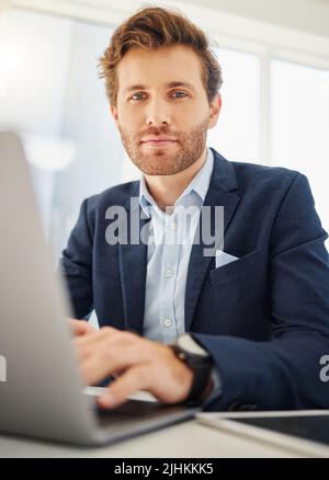 Porträt eines fokussierten jungen kaukasischen Geschäftsmannes, der in einem Büro an einem Laptop arbeitet. Selbstbewusster und ehrgeiziger männlicher Unternehmer im Internet Stockfoto