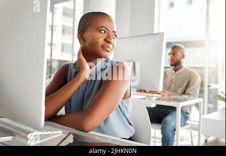 Junge gestresste Geschäftsfrau mit gemischter Rasse, die an Rückenschmerzen leidet, während sie allein am Arbeitsplatz an einem Laptop arbeitet. Eine unglückliche hispanische Geschäftsfrau, die arbeitet Stockfoto