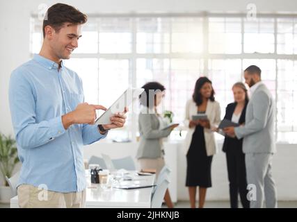 Junger glücklicher kaukasischer Geschäftsmann, der in einem Büro an einem digitalen Tablet arbeitet. Fröhlicher männlicher Chef, der Social Media auf einem digitalen Tablet hält und nutzt Stockfoto