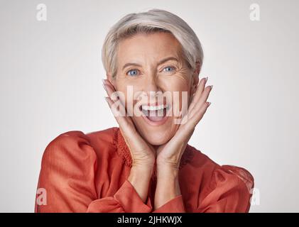 Porträt einer schönen kaukasischen reifen Frau isoliert vor einem grauen Studio-Hintergrund und Ausdruck Schock. Ältere Frau, die Gesichtsbehandlung macht Stockfoto