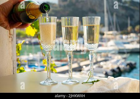 Drei Gläser französischen Champagner-Sekt und Blick auf bunte Fischerboote im alten Hafen von Cassis, Provence, Frankreich, Sommer Stockfoto