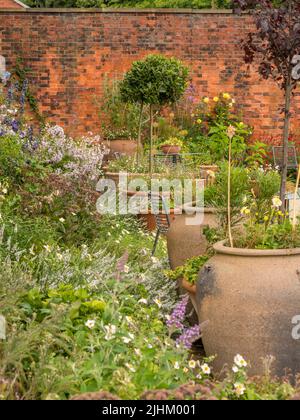 Große Pflanzgefäße mit Tischen und Stühlen dazwischen, im Bee and Butterfly Garden, RHS Bridgewater, Salford. VEREINIGTES KÖNIGREICH. Stockfoto