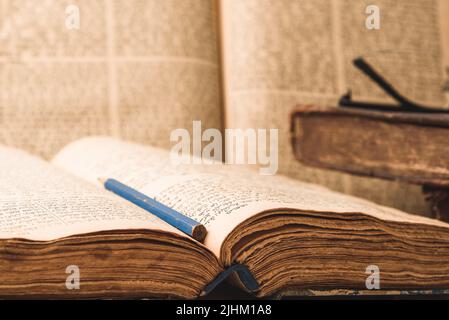 Alte abgenutzte, schäbige jüdische Bücher in Ledereinband und offene, verschwommene Tora im Hintergrund. Nahaufnahme. Selektiver Fokus Stockfoto